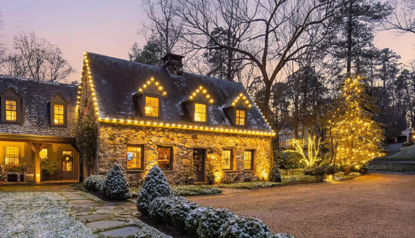 A beautifully decorated home glowing with Christmas lights, with snow-covered bushes adding to the festive holiday atmosphere